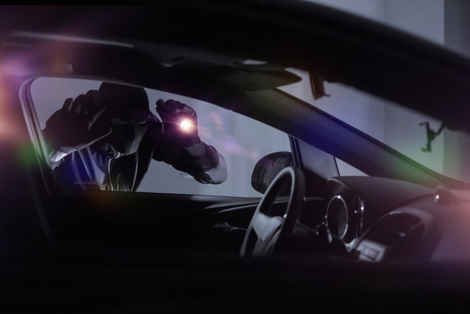 Dark figure with a flashlight looking into a vehicle with intent of car theft