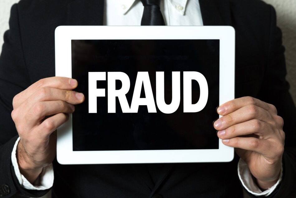 Closeup of man in suit holding a sign that says "Fraud"