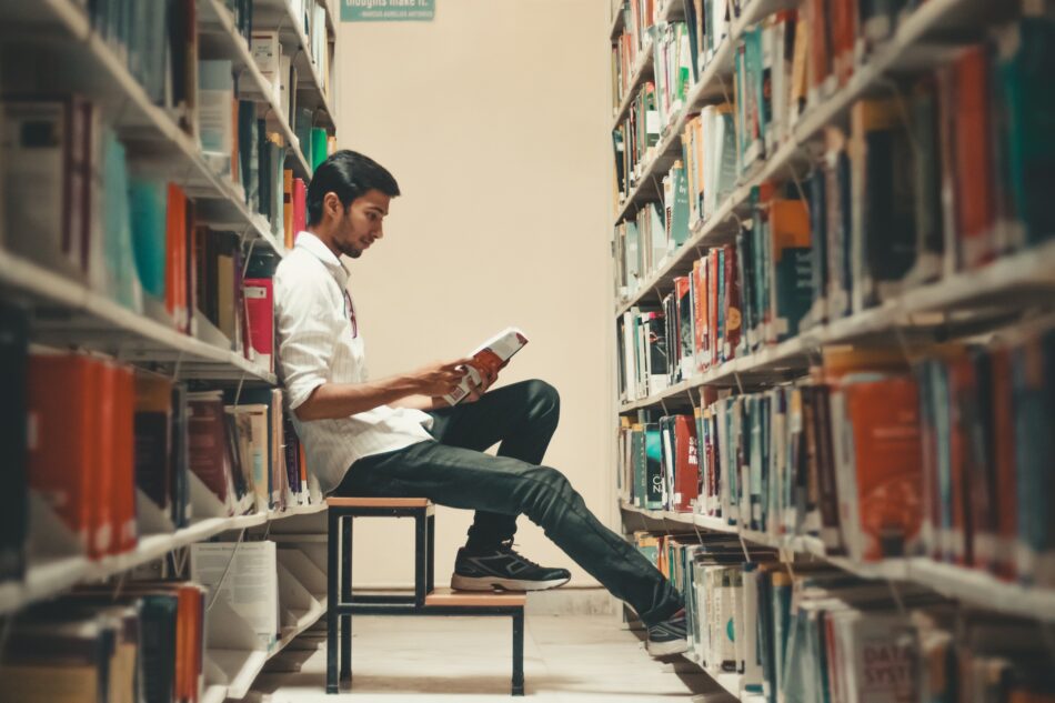 Man sitting in aisle of a library reading a book