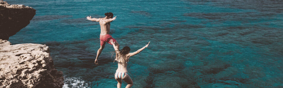 Back view of man and woman jumping into ocean off of a small cliff