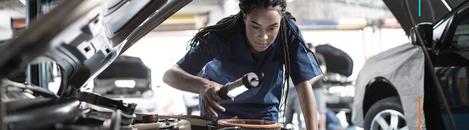 Mechanic looking under car hood with a light