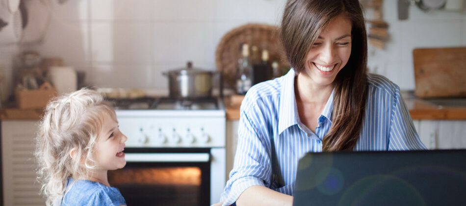 a mother smiling at her computer with her child beside her laughing