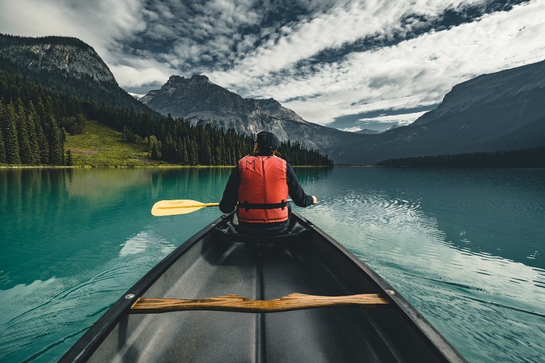 Man on canoe holding paddle and looking out at emerald lake and snow capped mountains