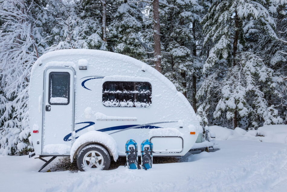 Small travel trailer parked in snowy forest for winter camping