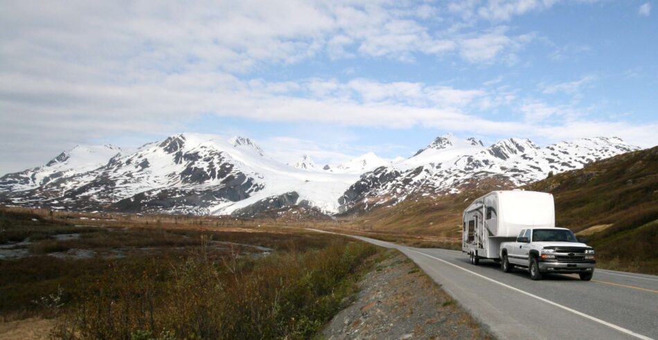 View of a truck on Canadian highway pulling a trailer with white-capped mountains in the background