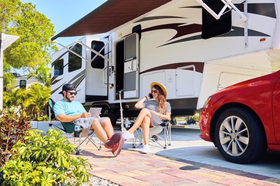 Couple sitting on lawn chairs outside of their RV on a sunny day