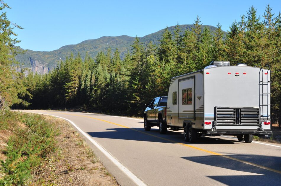 Vehicle pulling an RV on the highway through forest backdrop