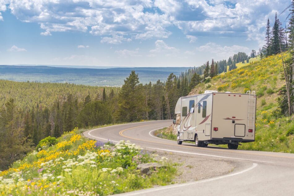 RV driving on a beautiful winding road among a mountainous summer terrain with blooming flowers along the roadside