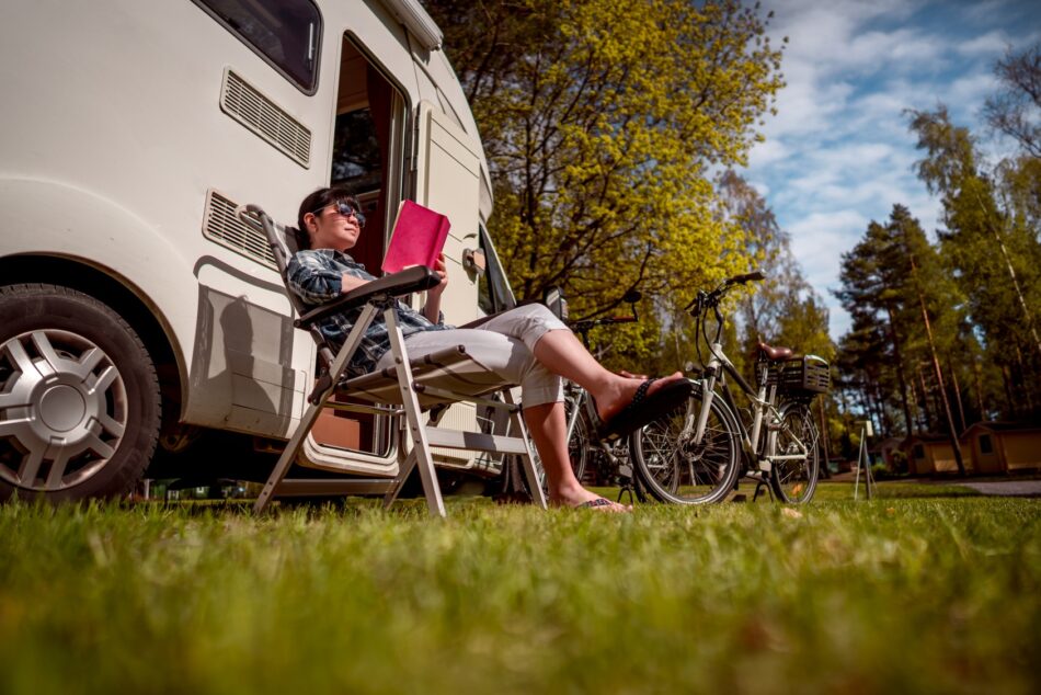 Person sitting on lawn chair outside of parked RV in field
