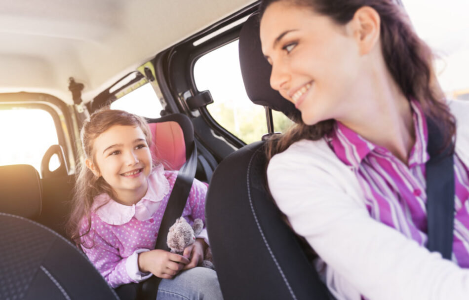Cute young girl in a car with her mother, they are sitting and smiling at each other