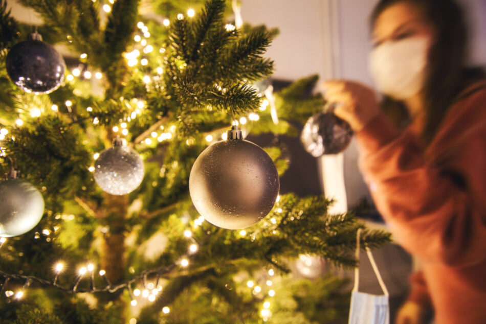 Young woman decorating a Christmas tree with medical safety mask for Covid-19, Coronavirus and Christmas concept, beautiful holiday background