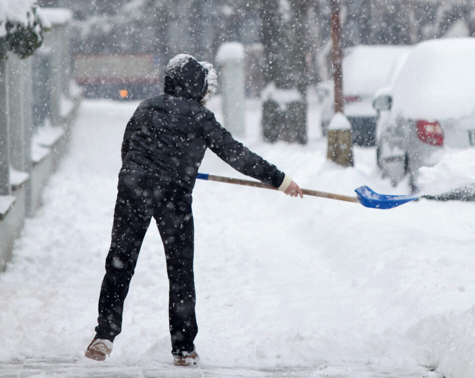 Woman shoveling snow from a sidewalk after a heavy snowfall in a city