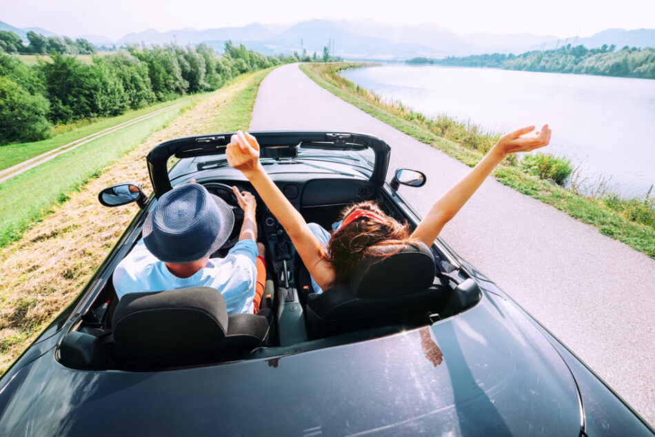 Couple driving along a body of water in a convertible