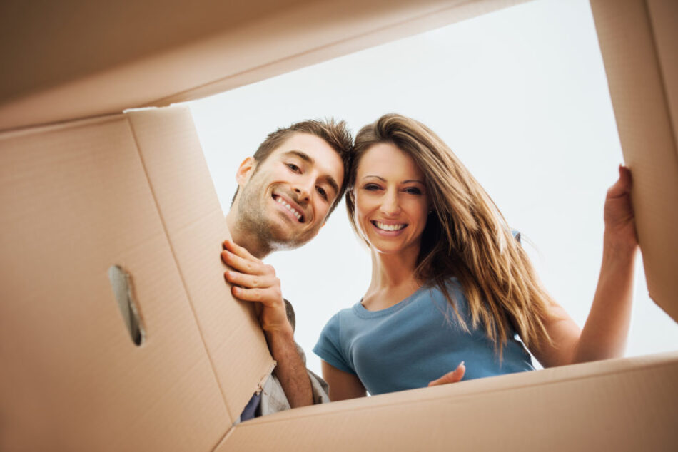 Smiling young couple opening a carton box and looking inside, relocation and unpacking concept