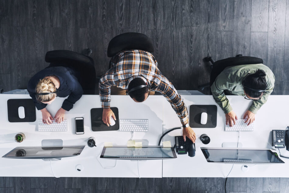 Overhead view of three workers in an office at their computers