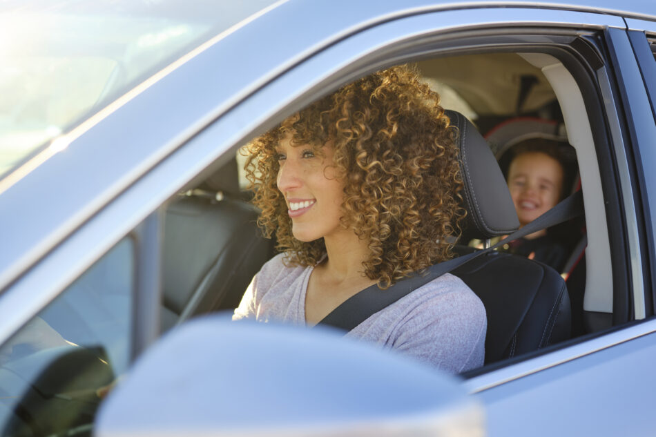 A woman driving in a car with a little boy in the backseat in a car seat.