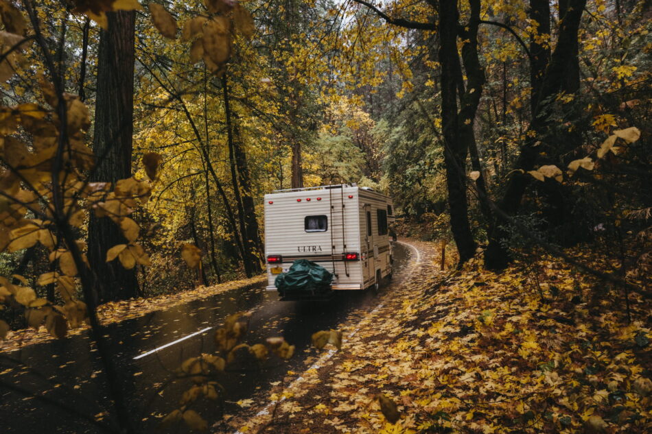 A motorhome driving through the rain on a windy forest road in autumn.