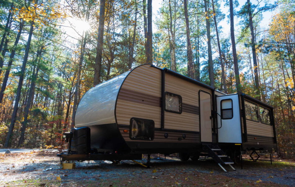 A large travel trailer parked at a forested campsite during fall.