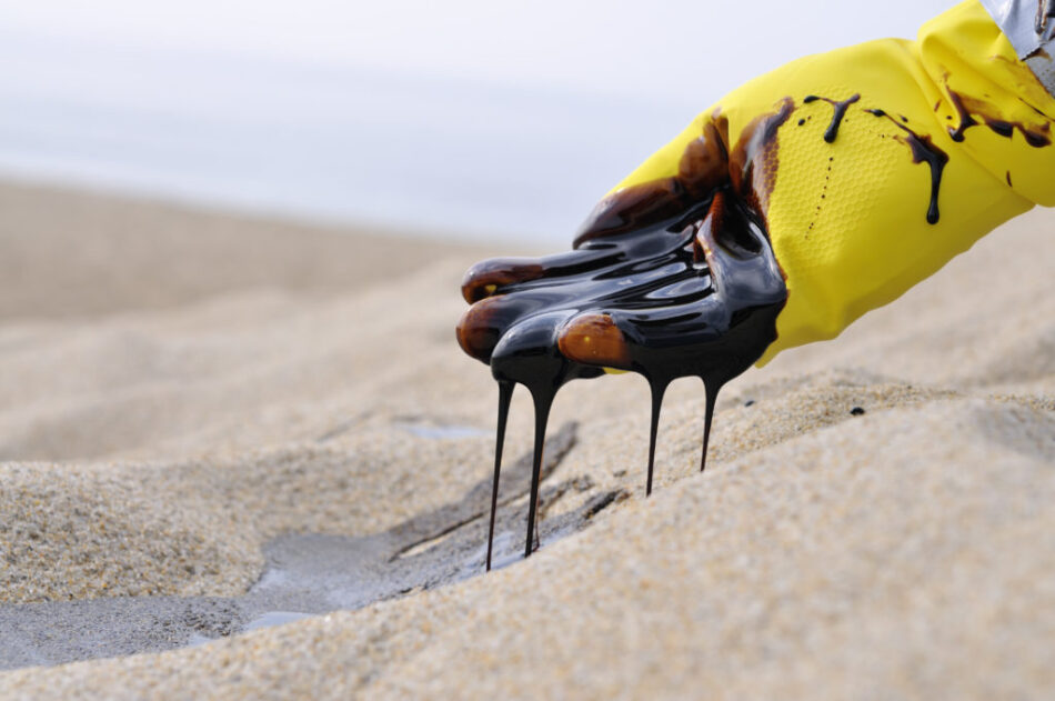 A gloved hand of unidentifiable/unnamed emergency worker scooping oil from pristine beach sand.