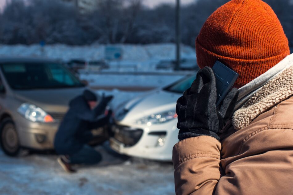 Over the shoulder view of someone on the phone in winter looking at two vehicles that were in an auto accident