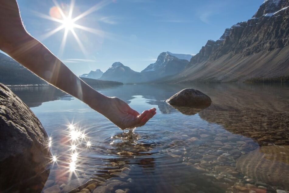 Human hand cupped to catch the fresh water from the lake, sunlight from sunset passing through the transparence of the water.