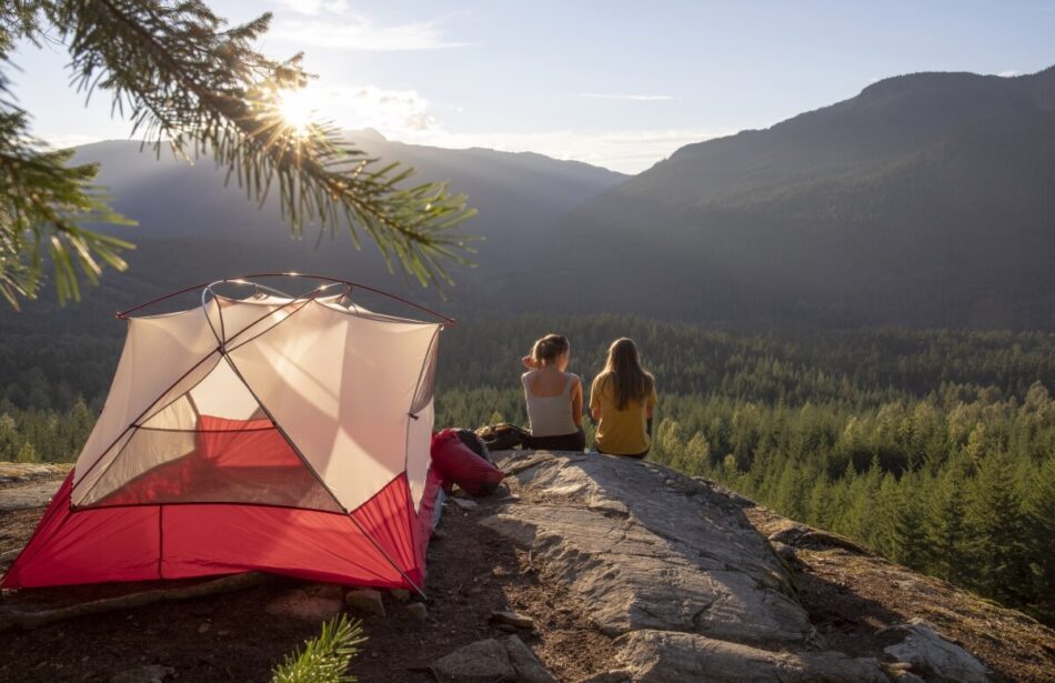 Private campground with friends sitting on mountain with tent beside it