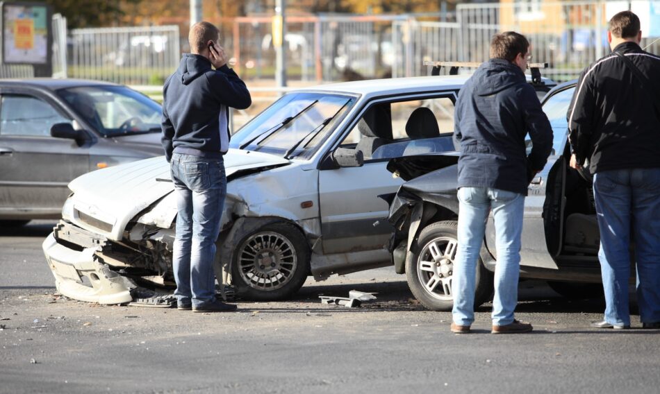 an uninsured driver on the phone with two other passengers standing by two totalled vehicles after a car accident