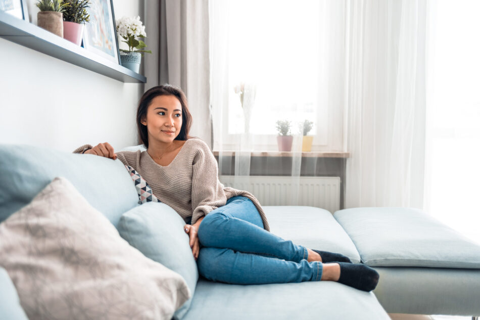Relaxed smiling asian woman sitting on sofa at home
