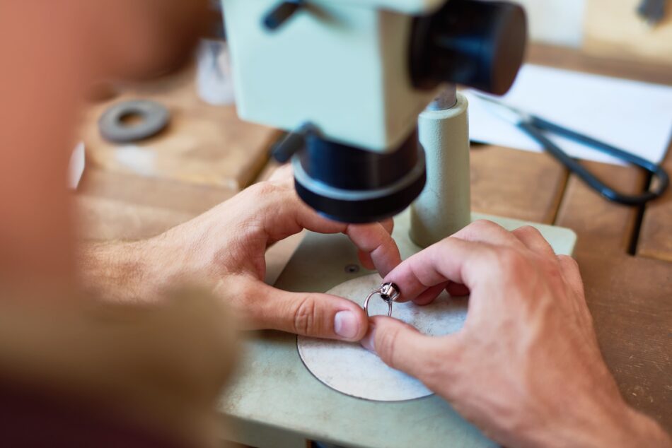 Hands holding a ring under a microscope for an appraisal for insurance