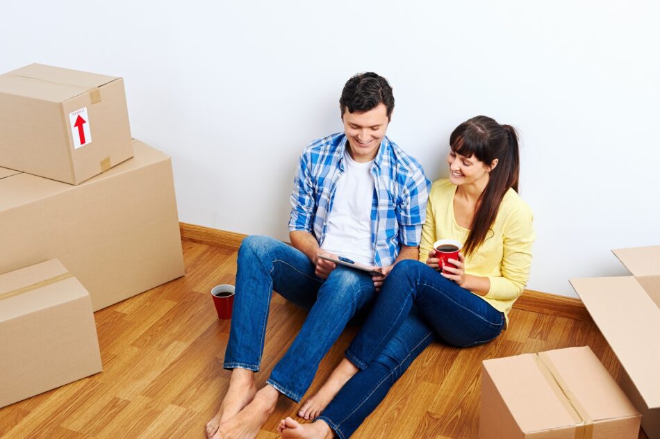 Young couple sitting on floor of empty house surrounded by boxes