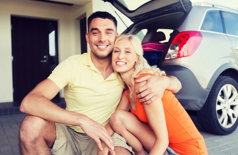 Young couple sitting in front of car smiling