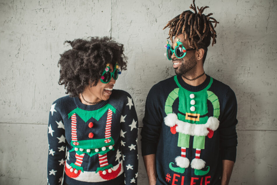 Young couple celebrating Christmas at home. They wear christmas sweaters and funny glasses.