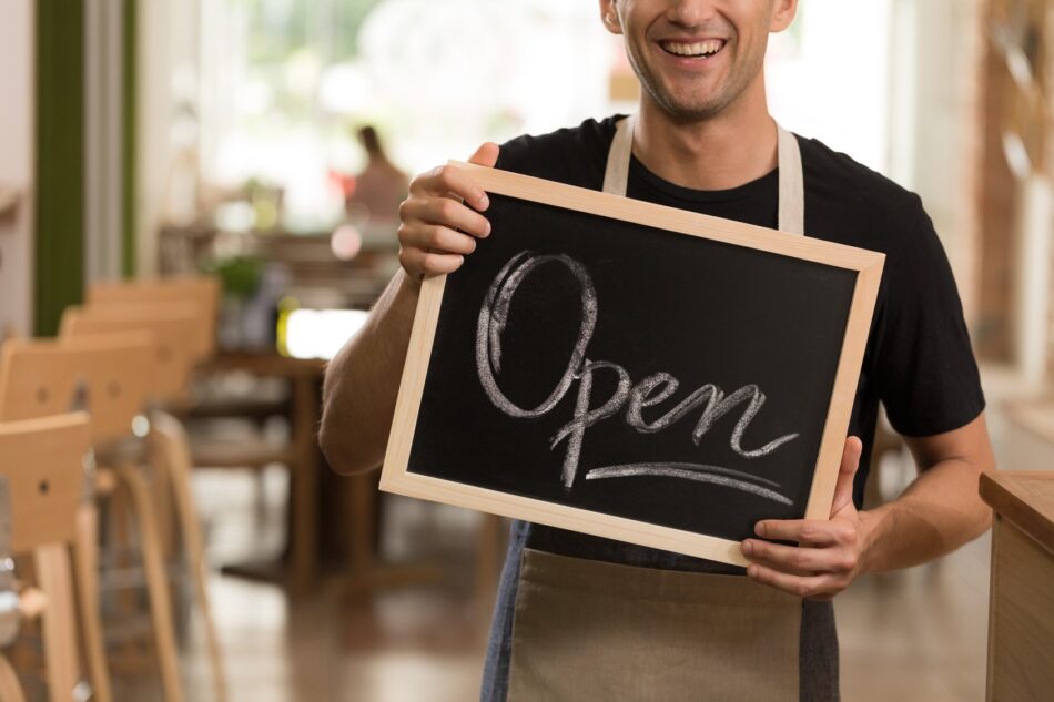 Closeup of hands holding a sign that says "Open"