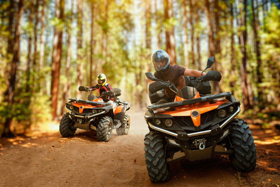 Two people riding OHVs on a dirt road through the forest