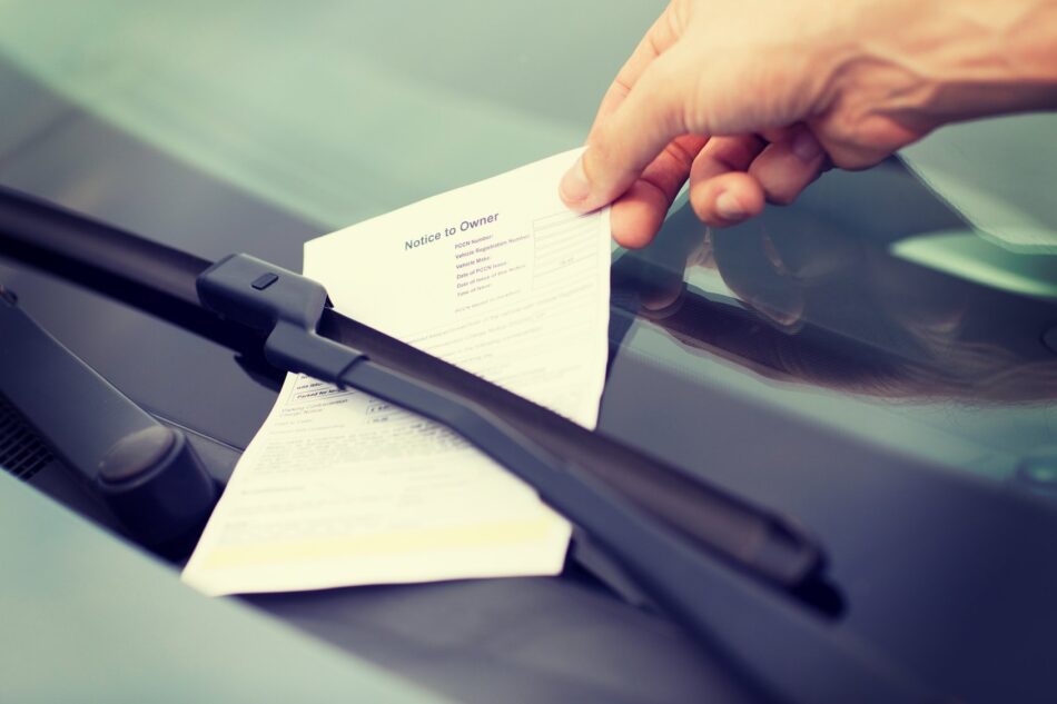Closeup of a hand placing a parking ticket under a windshield wiper