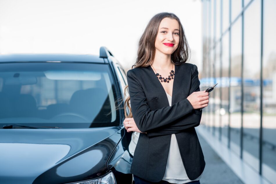a woman using her personal car for business, standing next to her place of work in a black blazer