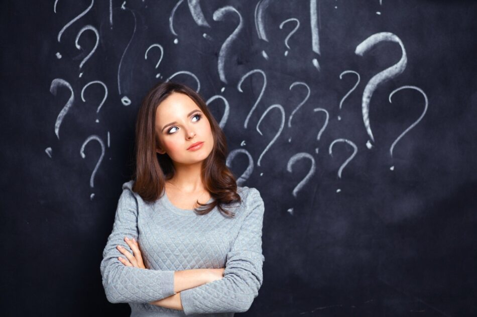 Woman standing in front of chalkboard with question marks drawn on top of it