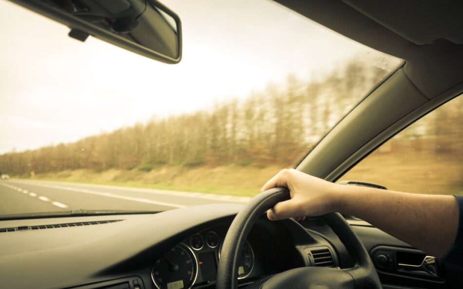 Closeup of hand on steering wheel driving down the highway