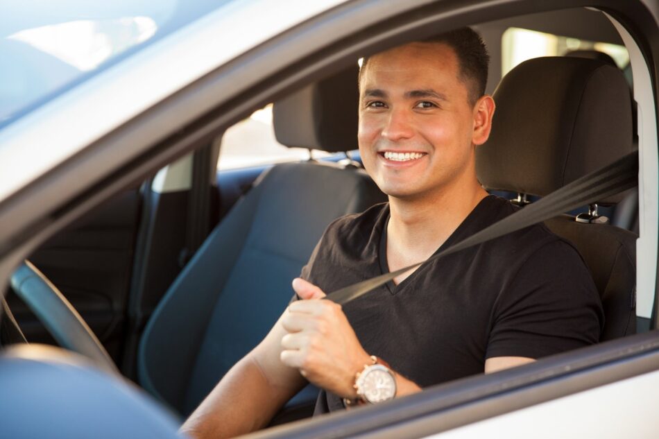 Young man in drivers seat looking out window and smiling