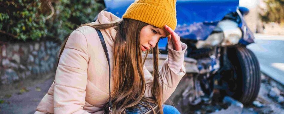 Woman sitting on sidewalk in front of car accident