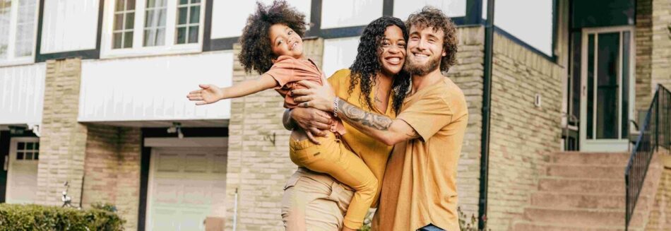 Young family hugging and smiling in front of home