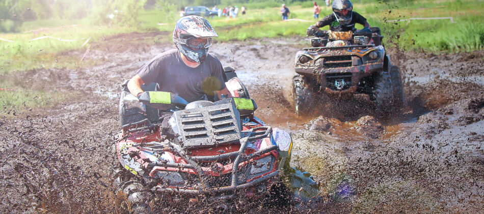 Two people riding ATV's through mud