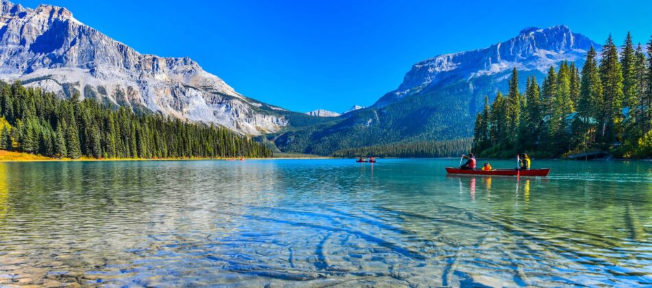 View of crystal clear lake with mountains in the background and a few canoes being rowed on the lake