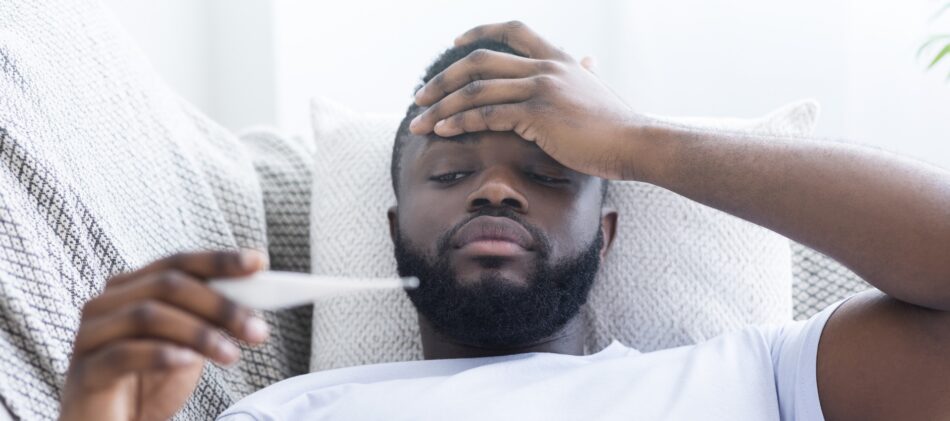 Man in bed on paid sick leave looking at thermometer after taking her temperature