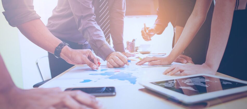 A bunch of business peoples hands pointing at different items on boardroom table
