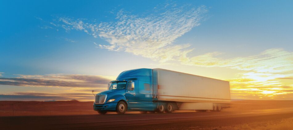 Commercial truck driving on highway at sunset