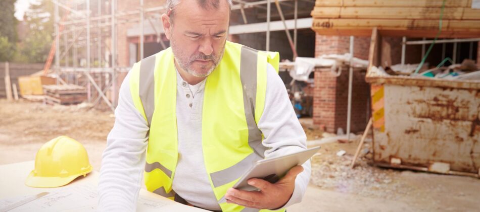 Man on construction site looking at plans on paper