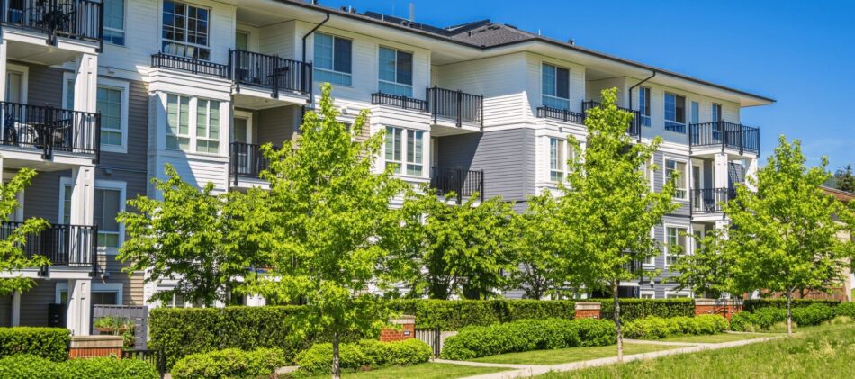 Exterior view of a condo building with lush green trees and landscaping