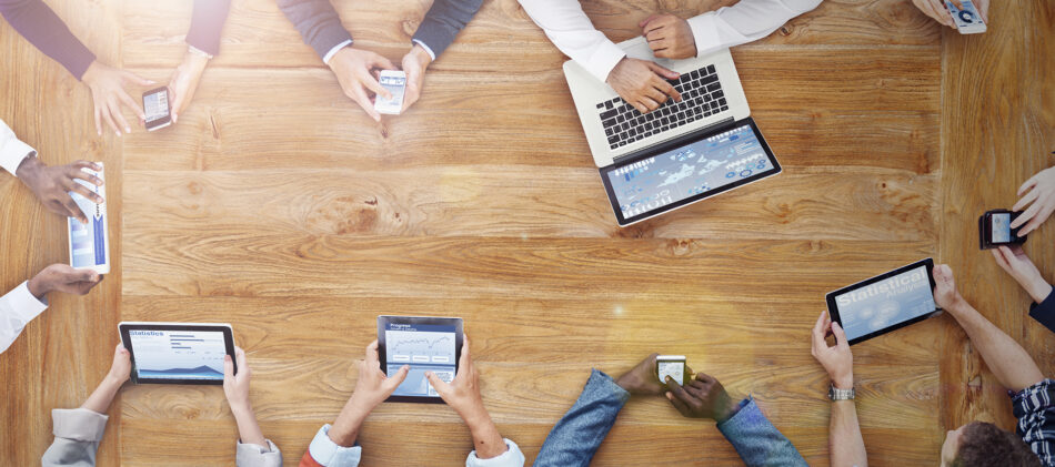 Overhead view of boardroom table and hands on devices