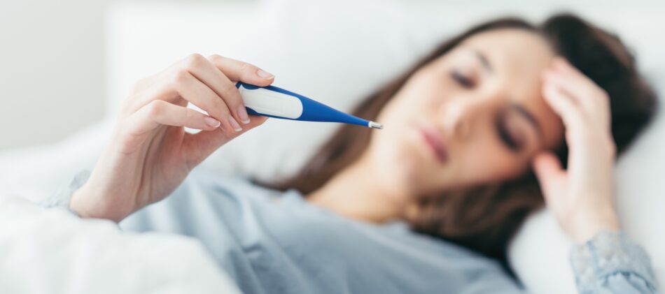 Woman in bed on paid sick leave looking at thermometer after taking her temperature